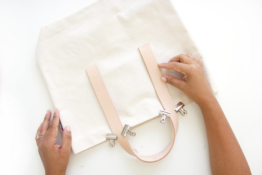 Transform a regular canvas tote bag into a DIY Leather Strap Canvas Tote Bag with the addition of leather and a few basic crafting supplies.